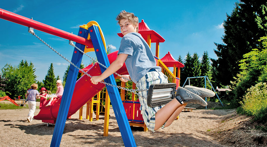 Ein junger Camingplatzgast beim Schaukeln auf dem Spielplatz